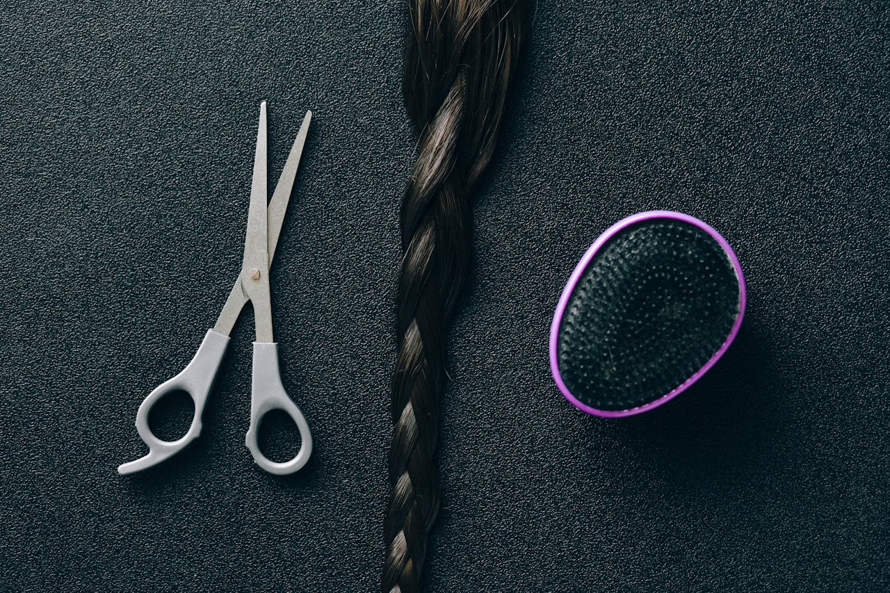 Close-up of hairdressing scissors, braided hair, and brush on black background.